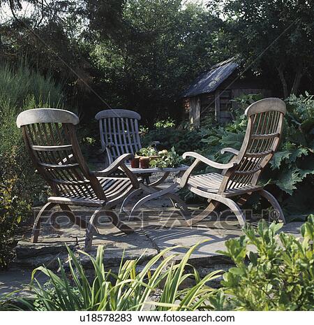 Stock Image - Wooden furniture on patio in country garden in summer. Fotosearch