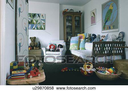 Wooden settle piled with cushions and soft toys in parrot-themed child's bedroom with white armchair View Large Photo Image Stock Photo - Wooden settle piled with cushions and soft toys in parrot-themed child's bedroom with white armchair. Fotosearch