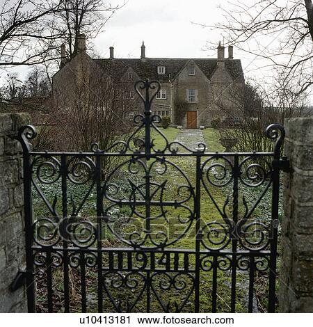Stock Image - Wrought iron gates and long path to traditional country house. Fotosearch