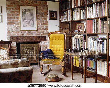 Yellow armchair and chess set on table in front of bookshelves in country living room with fireplace in exposed brick wall View Large Photo Image Stock Image - Yellow armchair and chess set on table in front of bookshelves in country living room with fireplace in exposed brick wall. Fotosearch