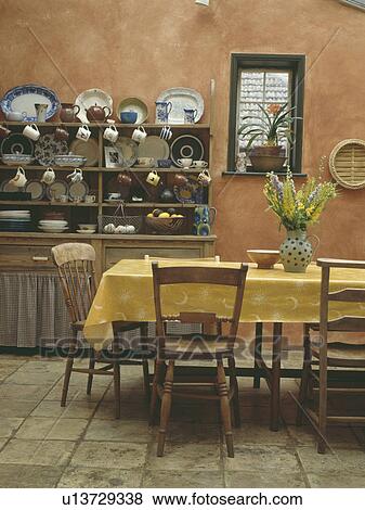 Yellow PVC cloth on table in kitchen with old pine chairs and dresser and stone flooring View Large Photo Image Stock Photo - Yellow PVC cloth on table in kitchen with old pine chairs and dresser and stone flooring. Fotosearch