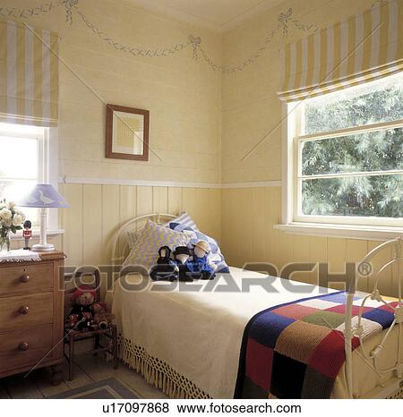 Stock Photo - Yellow striped blinds at window above white wrought iron single bed with knitted patchwork blanket and cream throw. Fotosearch