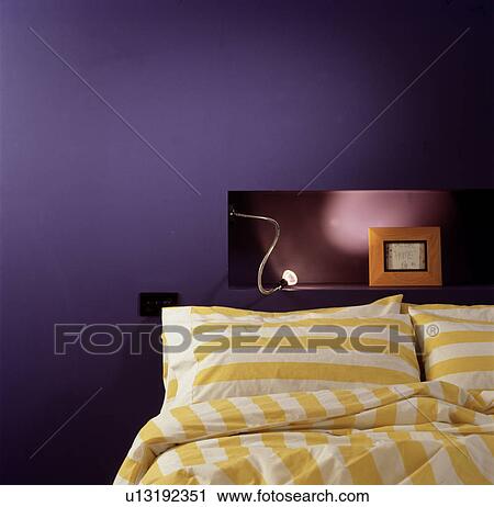 Yellow+white striped pillows and duvet on bed below light on alcove shelf in modern purple bedroom View Large Photo Image Stock Image - Yellow+white striped pillows and duvet on bed below light on alcove shelf in modern purple bedroom. Fotosearch