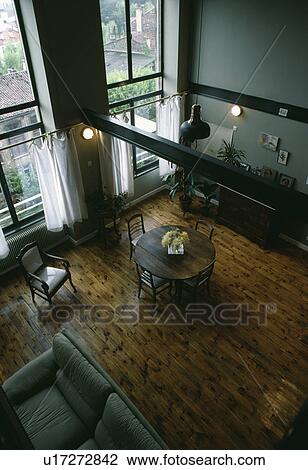 Stock Image - Aerial view of chairs and circular table in double height dining and living room with wooden flooring. Fotosearch