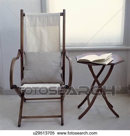 Stock Photography - Antique campaign chair with white cushions beside small octagonal table. Fotosearch