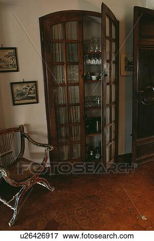 Stock Photo - Antique chair beside alcove cupboard with glazed doors in country hall. Fotosearch