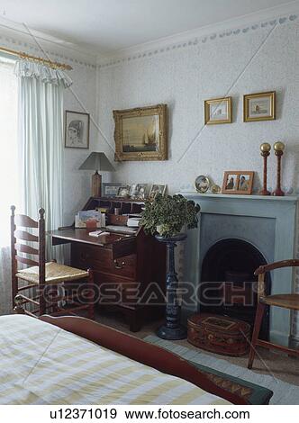 Antique desk and rush-seated ladderback chair in small bedroom with pale blue fireplace View Large Photo Image Stock Photo - Antique desk and rush-seated ladderback chair in small bedroom with pale blue fireplace. Fotosearch