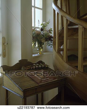 Stock Photo - Antique desk beside curved wooden staircase in country hall. Fotosearch