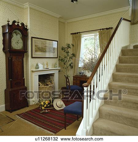 Antique longcase clock beside fireplace in country hall with cream stair carpet and neutral patterned wallpaper View Large Photo Image Stock Image - Antique longcase clock beside fireplace in country hall with cream stair carpet and neutral patterned wallpaper. Fotosearch
