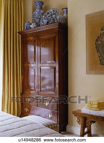 Stock Photograph - Antique oak linen press in traditional bedroom. Fotosearch