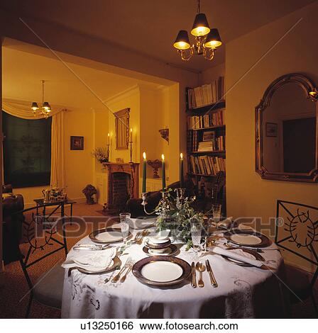 Stock Photograph - Antique plates and silver cutlery on circular table with white linen cloth in traditional dining room. Fotosearch