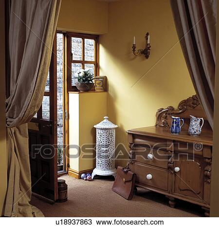 Antique white iron cylindrical stove beside open door in yellow hall with pine dresser and heavy beige silk curtains View Large Photo Image Stock Image - Antique white iron cylindrical stove beside open door in yellow hall with pine dresser and heavy beige silk curtains. Fotosearch