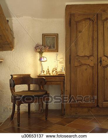 Stock Photo - Antique wooden chair and table with small lamp beside old carved wooden doors on cupboard. Fotosearch