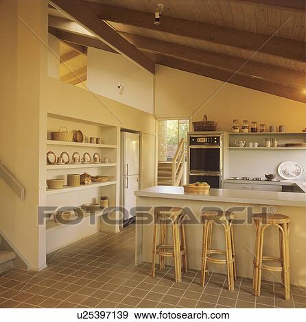 Bamboo stools at breakfast bar on island unit in modern neutral kitchen with tiled floor View Large Photo Image Stock Photo - Bamboo stools at breakfast bar on island unit in modern neutral kitchen with tiled floor. Fotosearch