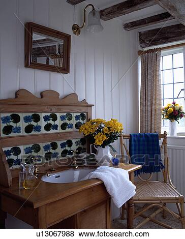 Basin set into old pine washstand with Blue+white tiles in panelled white cottage bathroom with bamboo+cane chair View Large Photo Image Stock Photo - Basin set into old pine washstand with Blue+white tiles in panelled white cottage bathroom with bamboo+cane chair. Fotosearch