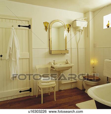 Bathrobe hanging on back of door in cream bathroom with towels on old cream chair beside wall-mounted basin View Large Photo Image Stock Photograph - Bathrobe hanging on back of door in cream bathroom with towels on old cream chair beside wall-mounted basin. Fotosearch