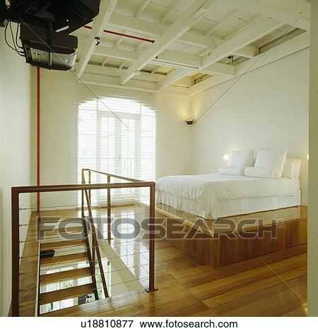 Bed with white linen and pillows on raised wooden platform above wooden flooring in modern loft conversion bedroom View Large Photo Image Stock Photo - Bed with white linen and pillows on raised wooden platform above wooden flooring in modern loft conversion bedroom. Fotosearch