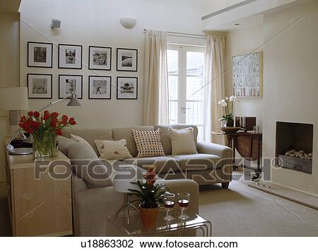Stock Image - Beige sofas and framed black+white photographs in cream contemporary living room. Fotosearch