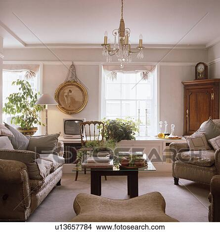 Beige sofas and green houseplants in townhouse living room with small glass chandelier above glass-topped coffee table View Large Photo Image Picture - Beige sofas and green houseplants in townhouse living room with small glass chandelier above glass-topped coffee table. Fotosearch