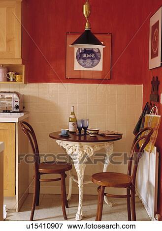 Stock Photo - Bentwood Thonet chairs and small circular Victorian-style table in corner of red kitchen with white wall tiles. Fotosearch