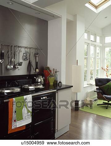 Black Aga in modern kitchen extension with metal utensils on stainless steel wall above oven View Large Photo Image Stock Photo - Black Aga in modern kitchen extension with metal utensils on stainless steel wall above oven. Fotosearch