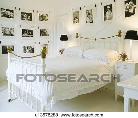 Stock Photo - Black and white photographs on the walls of white bedroom with black lamps on either side of antique brass bed. Fotosearch