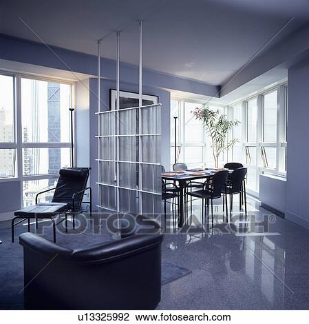 Stock Image - Black leather chaiselongue and armchair in openplan grey living and dining room with divider and grey flooring. Fotosearch