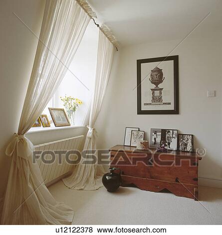 Stock Photo - Black & white engraving above antique wooden chest in attic room with white voile curtains beside radiator. Fotosearch