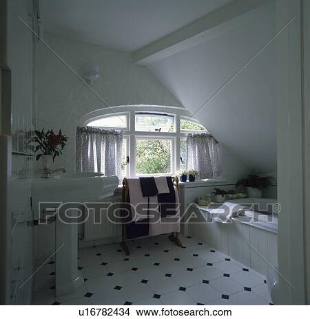 Picture - Black+white chequerboard tiled floor in white attic bathroom with curved window and pedestal basin. Fotosearch