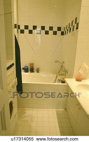 Black+white tiled border on wall above bath in modern white tiled bathroom with washing machine View Large Photo Image Stock Photography - Black+white tiled border on wall above bath in modern white tiled bathroom with washing machine. Fotosearch