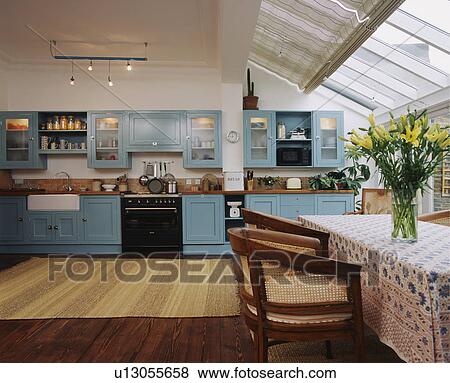 Blind on glass roof in modern white kitchen dining room with range oven and pastel blue fitted cupboards View Large Photo Image Stock Photo - Blind on glass roof in modern white kitchen dining room with range oven and pastel blue fitted cupboards . Fotosearch