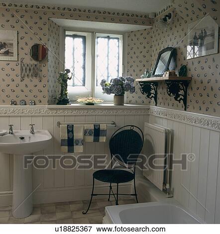 Stock Photo - Blue and white wallpaper and metal chair in cottage bathroom with white raised tile border above white panelling . Fotosearch