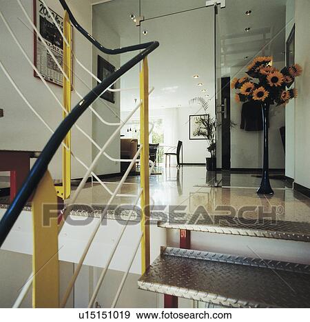 Stock Photo - Blue and yellow metal bannisters on staircase with metal treads up to modern hall with sunflowers in tall vase. Fotosearch