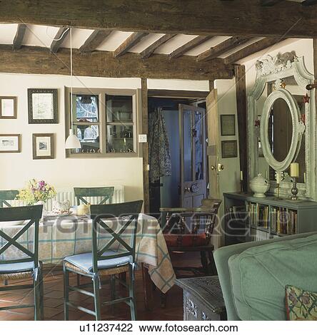 Stock Image - Blue chairs and checked cloth on table in cottage dining room with beamed ceiling. Fotosearch