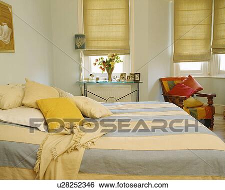 Blue+cream striped bedcover and yellow cushions on bed in bedroom with cream blinds at windows View Large Photo Image Stock Photograph - Blue+cream striped bedcover and yellow cushions on bed in bedroom with cream blinds at windows. Fotosearch