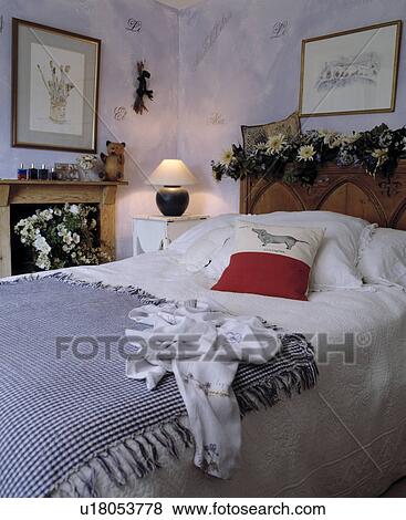 Blue+white checked throw and white linen on carved bed with dried flower garland in mauve cottage bedroom View Large Photo Image Stock Photo - Blue+white checked throw and white linen on carved bed with dried flower garland in mauve cottage bedroom. Fotosearch