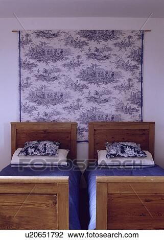 Stock Image - Blue+white Toile de Jouy fabric on wall behind old pine twin beds with blue linen and Toile de Jouy pillows. Fotosearch