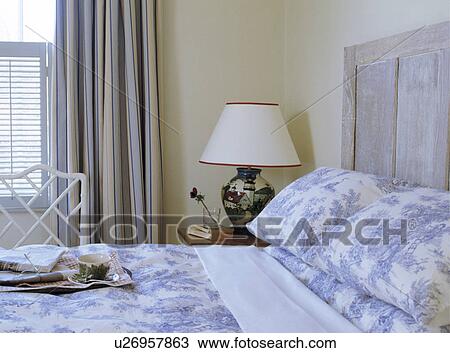 Blue+white Toile de Jouy pillows and quilt on limed wood bed in bedroom with cream+blue striped curtains and white lamp View Large Photo Image Stock Image - Blue+white Toile de Jouy pillows and quilt on limed wood bed in bedroom with cream+blue striped curtains and white lamp. Fotosearch
