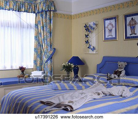 Blue+yellow striped quilt and pillows on bed in neutral bedroom with white net and blue+yellow floral curtains View Large Photo Image Stock Photograph - Blue+yellow striped quilt and pillows on bed in neutral bedroom with white net and blue+yellow floral curtains. Fotosearch