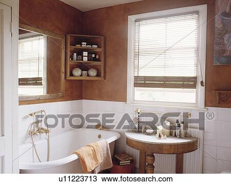 Stock Image - Brown sponge-effect walls above white tiles in bathroom with rolltop bath and small marble-topped antique table. Fotosearch