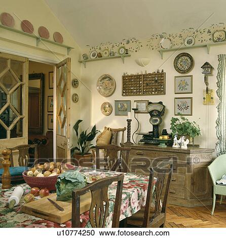 Stock Image - Cabbage and chopping board on table with floral cloth in dining room with glazed pine doors and display shelves on the walls. Fotosearch