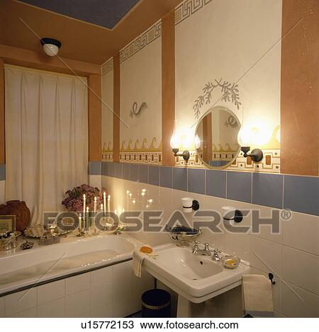 Candles on the side of bath in small bathroom with lighted lamps above basin and white wall tiles with blue tiled border View Large Photo Image Stock Image - Candles on the side of bath in small bathroom with lighted lamps above basin and white wall tiles with blue tiled border. Fotosearch