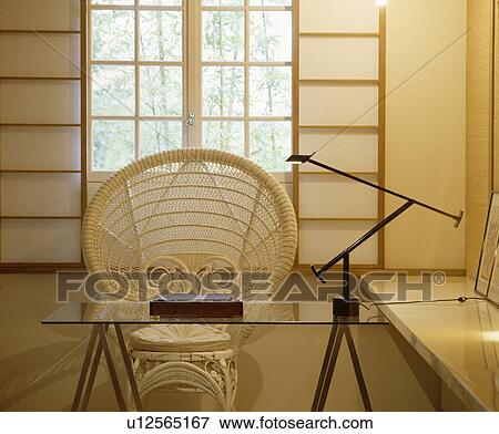 Stock Photo - Cane peacock chair and glass trestle table in modern oriental-style study. Fotosearch