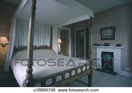 Stock Photograph - Carved four-poster bed with white canopy in bedroom with old television in fireplace. Fotosearch