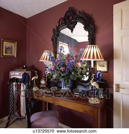 Carved mahogany mirror above antique table with lighted lamps and fresh floral arrangement in red bedroom View Large Photo Image Stock Image - Carved mahogany mirror above antique table with lighted lamps and fresh floral arrangement in red bedroom. Fotosearch