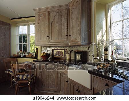 Carved wood doorson cupboards in traditional country kitchen with white ceramic butler's sink in front of window View Large Photo Image Picture - Carved wood doorson cupboards in traditional country kitchen with white ceramic butler's sink in front of window. Fotosearch