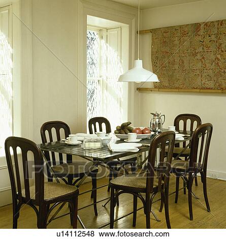 Chairs with cane seats at table with white crockery in white dining room with white pendant light View Large Photo Image Stock Photo - Chairs with cane seats at table with white crockery in white dining room with white pendant light. Fotosearch