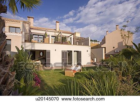 Stock Image - Chaiselongue on lawn in front of modern Spanish villa with balconies and patio doors. Fotosearch