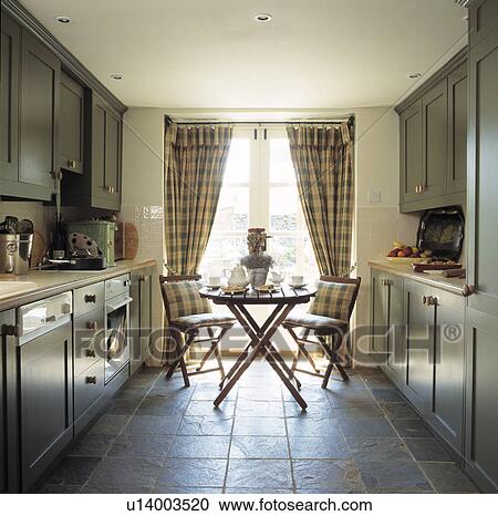 Checked curtains and cushions on chairs with circular table in kitchen with grey fitted cupboards and slate floor tiles View Large Photo Image Stock Image - Checked curtains and cushions on chairs with circular table in kitchen with grey fitted cupboards and slate floor tiles. Fotosearch