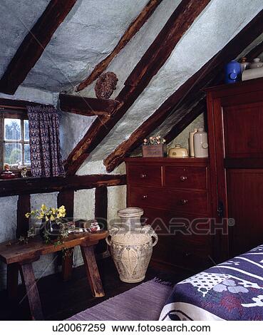 Chest-of-drawers below sloping ceiling in dark attic bedroom with large ceramic pot beside wooden stool View Large Photo Image Stock Photo - Chest-of-drawers below sloping ceiling in dark attic bedroom with large ceramic pot beside wooden stool. Fotosearch